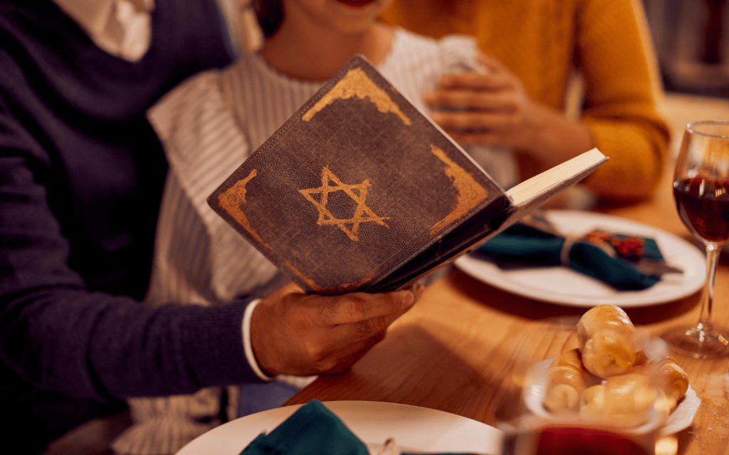 Dłonie trzymające modlitewnik z Gwiazdą Dawida przy nakrytym stole podczas szabatu