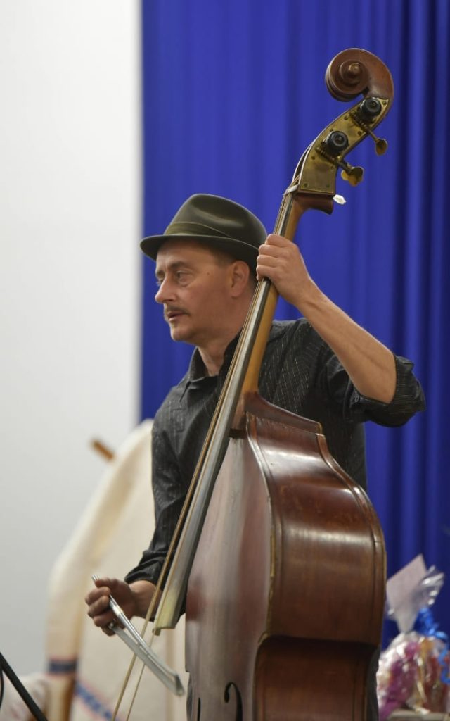 Mężczyzna grający na kontrabasie na tle niebieskiej zasłony