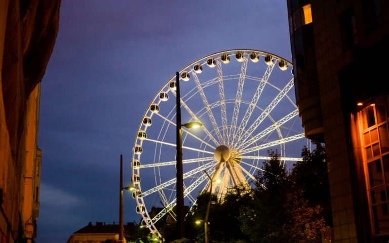 Podświetlony diabelski młyn między kamienicami podczas Sziget Festival w Budapeszcie o zmierzchu