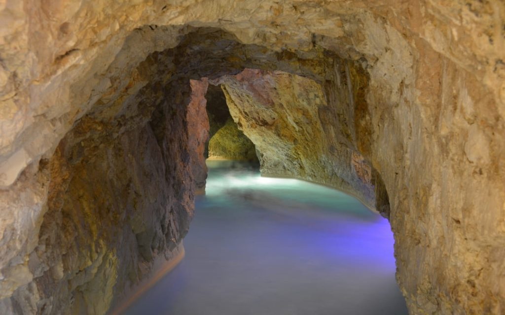 Skalne tunele Jaskini Termalnej Miskolctapolca z turkusową wodą i fioletowym podświetleniem