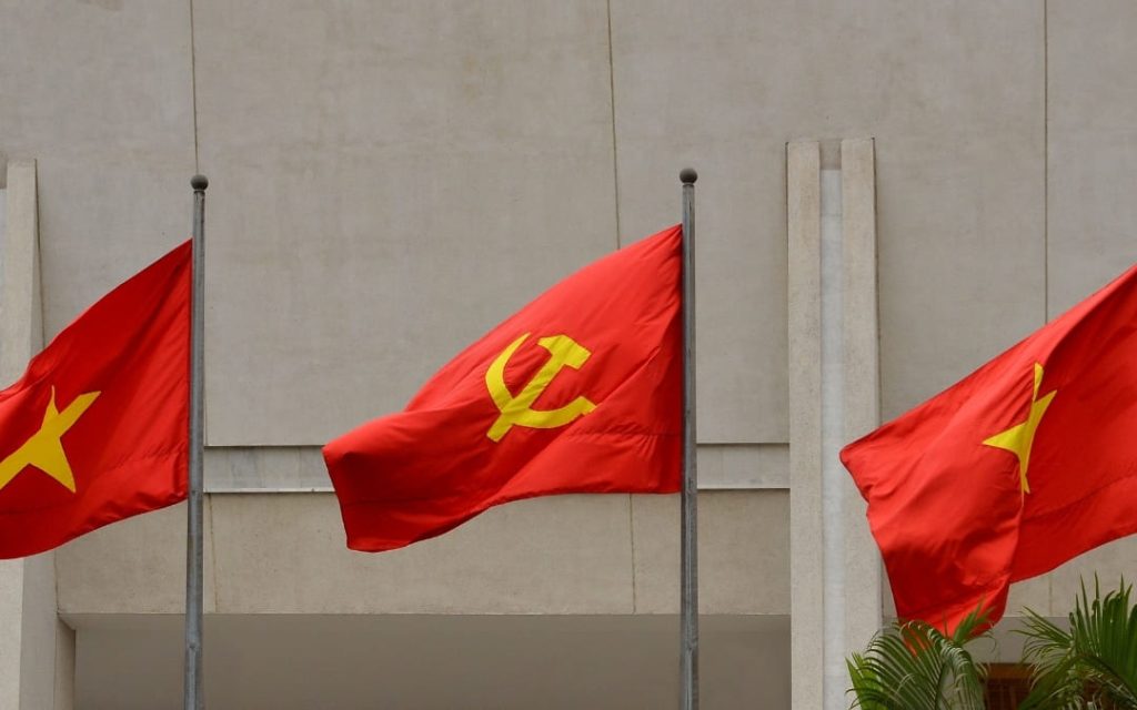 Trzy czerwone flagi z żółtymi symbolami powiewające na masztach przed budynkiem