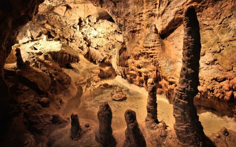 Wysokie stalagmity i stalaktyty przy podziemnym jeziorku w Jaskini Pál-völgyi w Budapeszcie