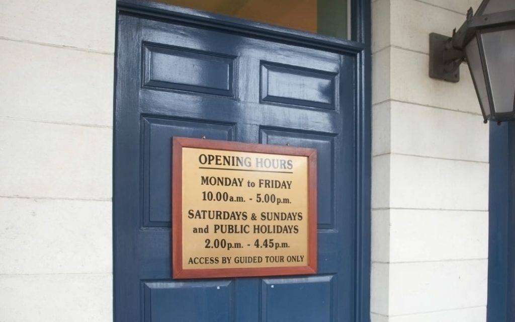 Złota tabliczka z godzinami otwarcia na granatowych drzwiach wejściowych muzeum lub atrakcji