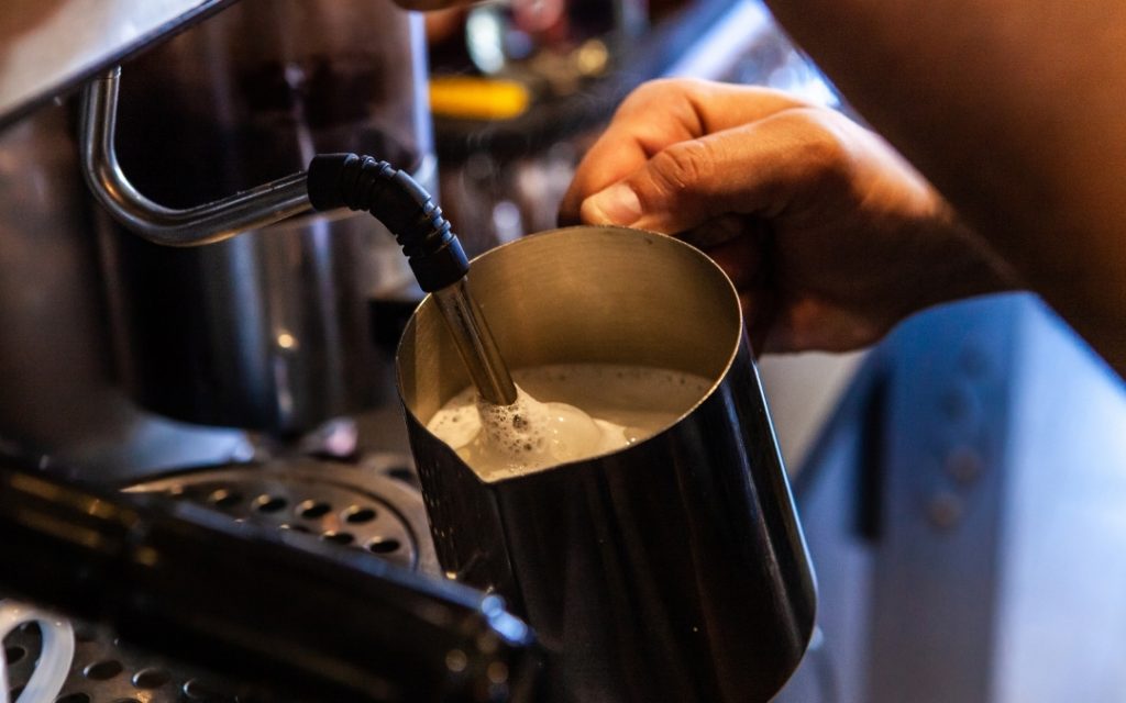Barista spieniający mleko w czarnym dzbanku przy ekspresie do kawy