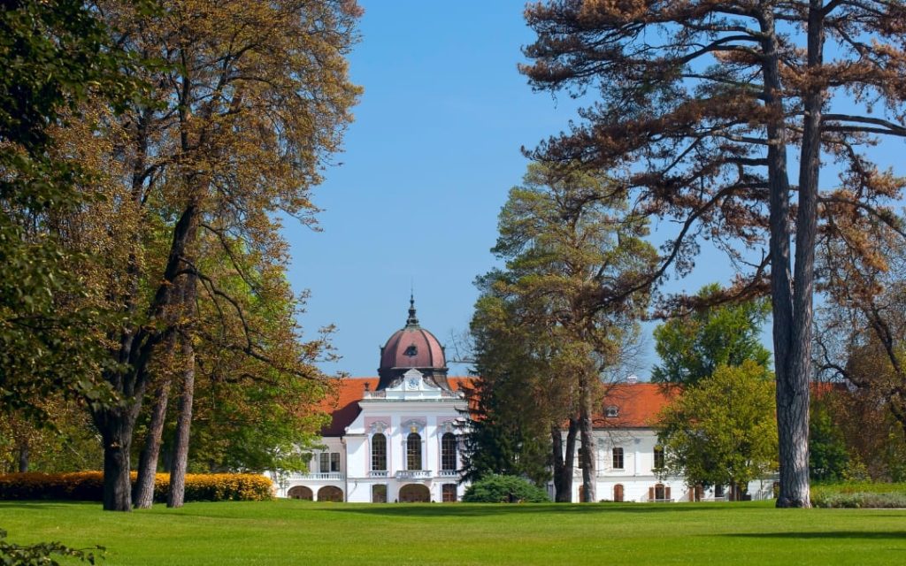 Barokowy Pałac Królewski w Gödöllő widziany przez drzewa parkowe w słoneczny dzień