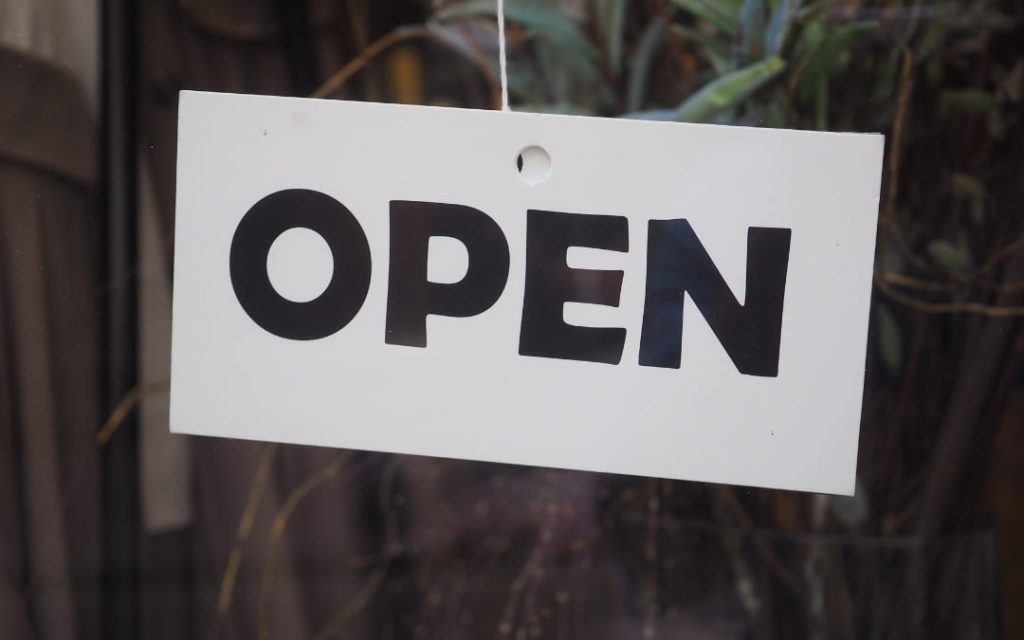 Biała tabliczka z napisem _Open_ zawieszona na szybie drzwi wejściowych