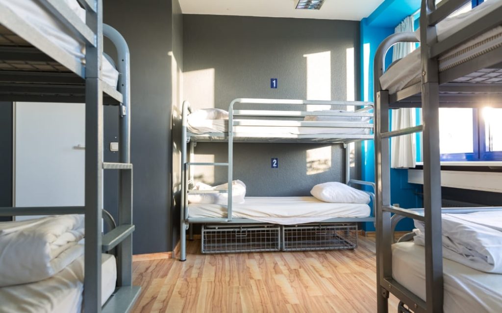 Pokój hostelowy z szarymi łóżkami piętrowymi i metalowymi konstrukcjami