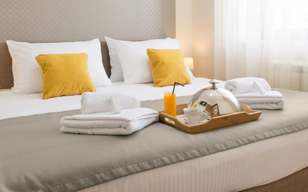 Schludny pokój hotelowy z białą pościelą i żółtymi poduszkami dekoracyjnymi