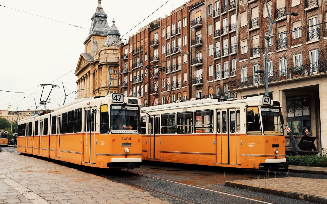 Dwa żółte tramwaje linii 47 stojące obok siebie na ulicy w Budapeszcie, na tle kamienic i zabytkowego budynku