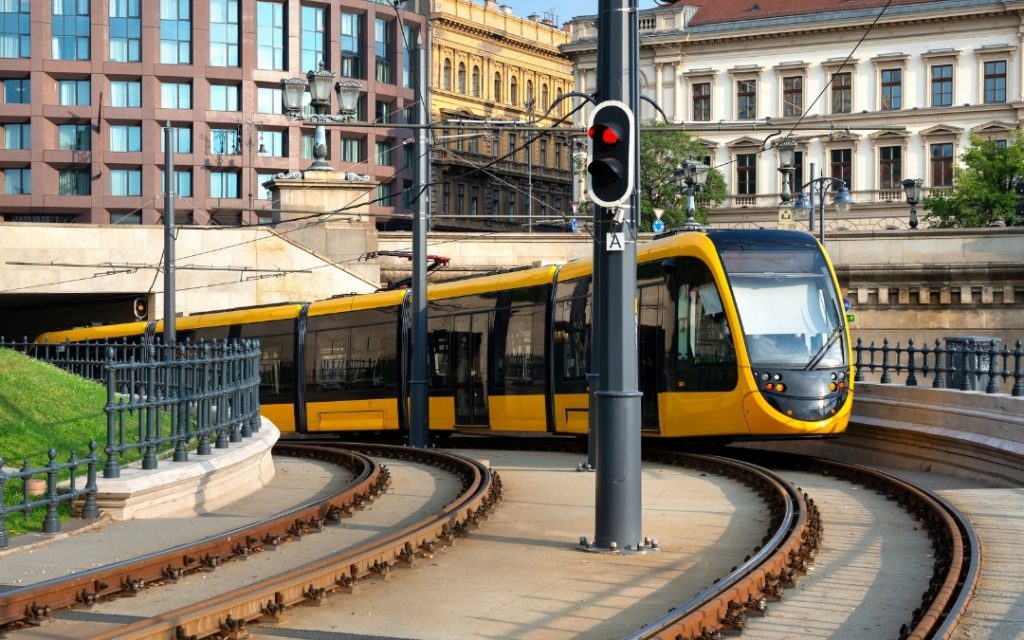 Nowoczesny żółty tramwaj skręcający na zakręcie torów w centrum Budapesztu, przy historycznych kamienicach