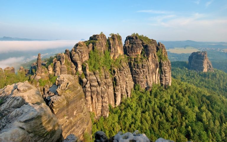 Panorama skalnych formacji Parku Narodowego Saskiej Szwajcarii z wysokimi piaskowcowymi ostańcami wznoszącymi się ponad rozległym lasem