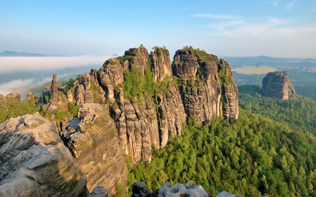 Panorama skalnych formacji Parku Narodowego Saskiej Szwajcarii z wysokimi piaskowcowymi ostańcami wznoszącymi się ponad rozległym lasem