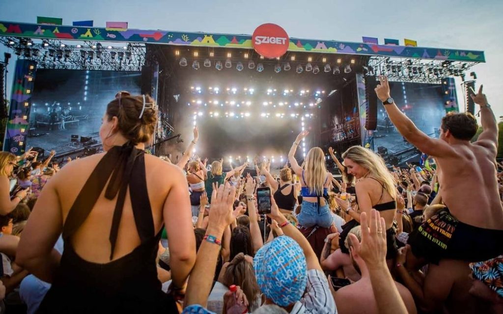 Publiczność bawiąca się pod główną sceną festiwalu Sziget w Budapeszcie, z widocznymi światłami reflektorów i tłumem ludzi unoszących ręce w rytm muzyki