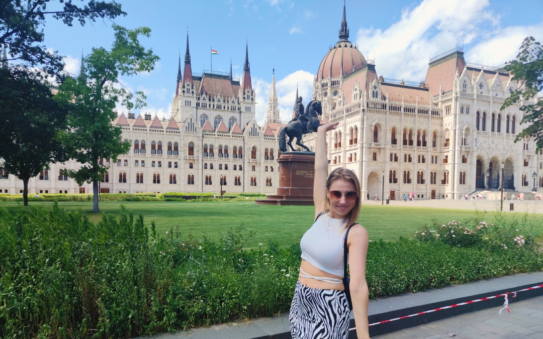 Turystka w słoneczny dzień robiąca sobie zdjęcie z Parlamentem w Budapeszcie