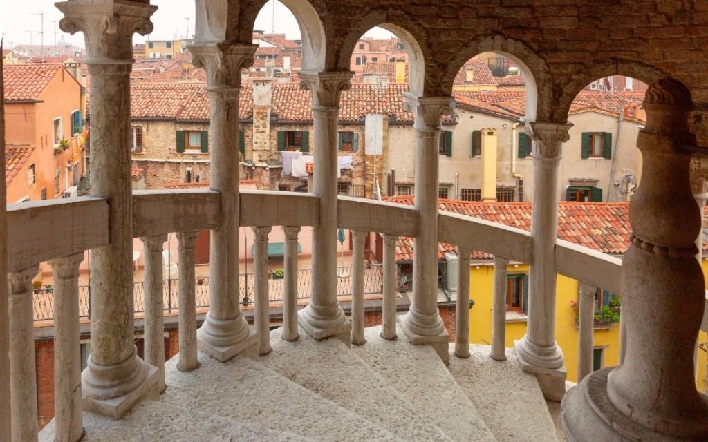 Kamienne, spiralne schody Scala Contarini del Bovolo w Wenecji. Widok z łukowej loggii na gęsto zabudowane dachy i kamienice.