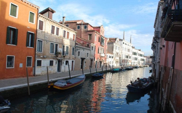 Kanał w dzielnicy Cannaregio w Wenecji. Wzdłuż wody zacumowane łodzie, a za nimi ciąg kolorowych kamienic odbijających się w spokojnej wodzie.