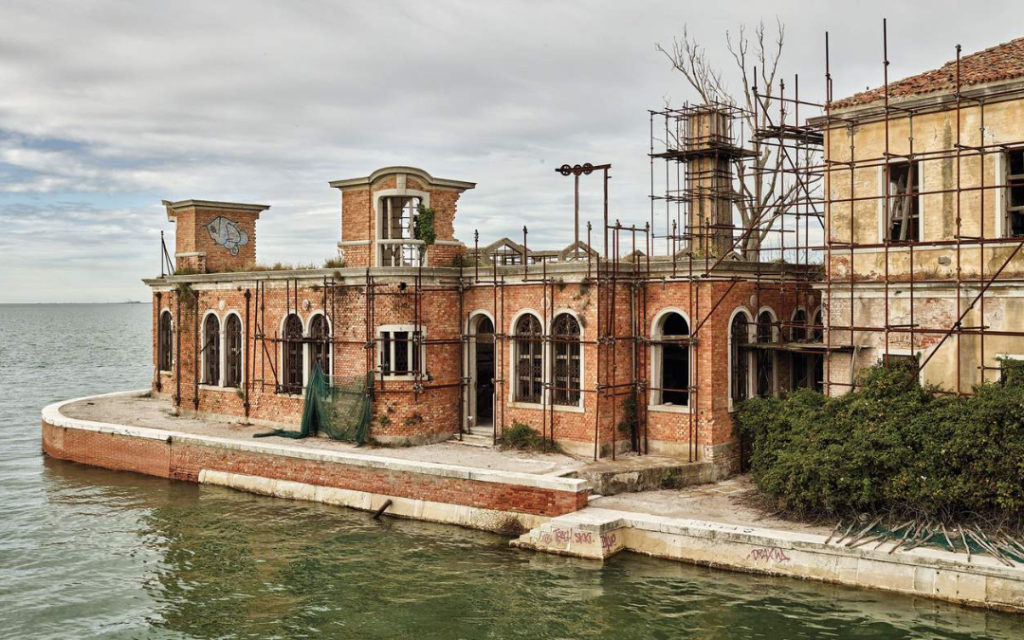 Opuszczony budynek na wyspie Poveglia. Zrujnowana, ceglana konstrukcja z łukowymi oknami, otoczona wodą Laguny. Widoczne rusztowania.