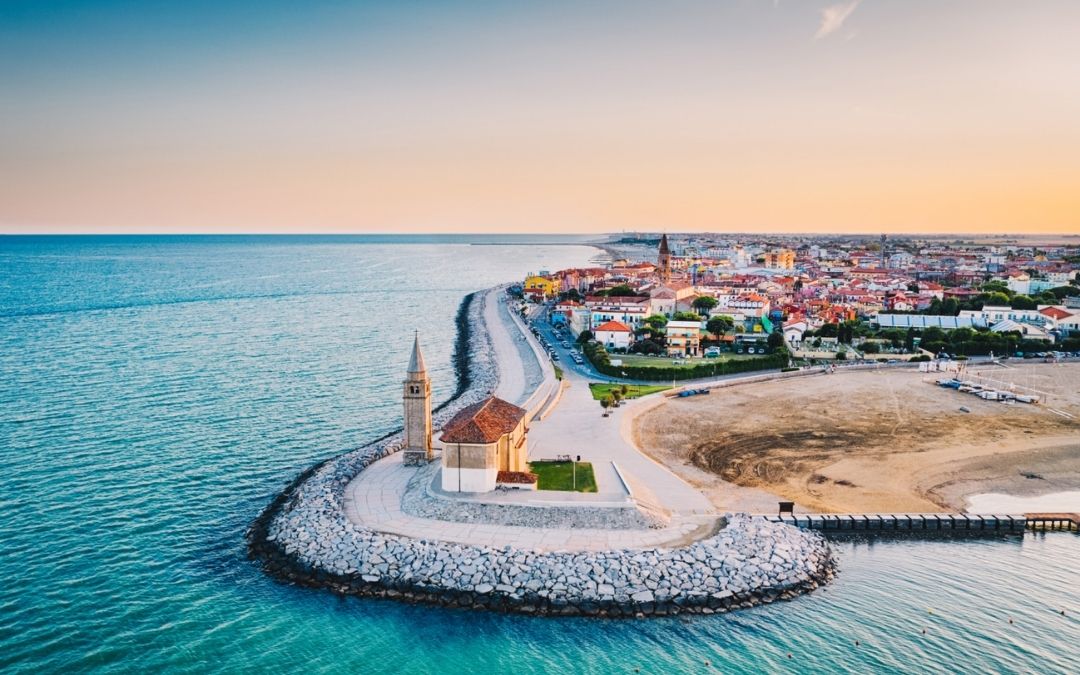 Caorle z lotu ptaka. Kościół Madonna dell'Angelo i dzwonnica na falochronie, obok plaży i kolorowego historycznego miasteczka.