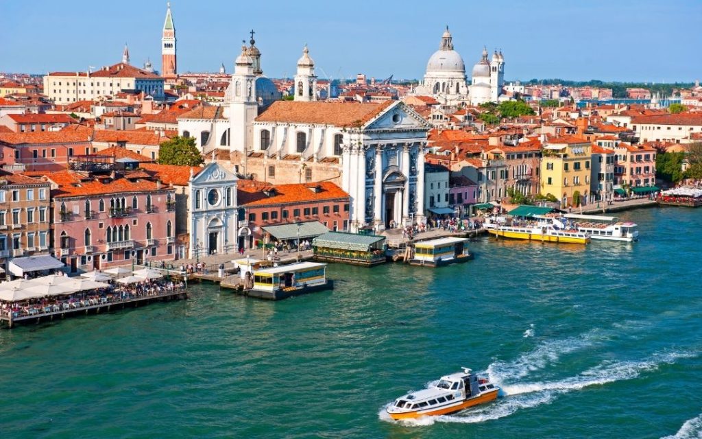 Panorama weneckiej dzielnicy Dorsoduro. Z lotu ptaka widać Grand Canal, kolorowe kamienice i kościoły oraz motorówkę na pierwszym planie.