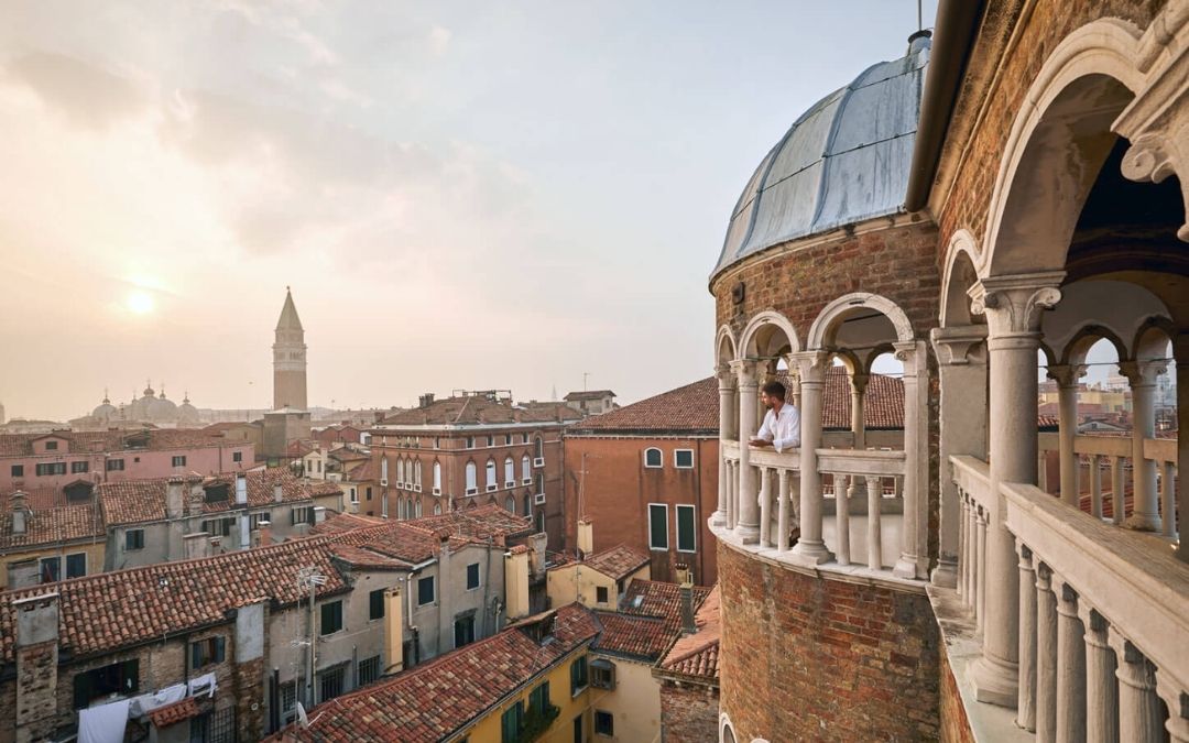 Panoramiczny widok na dachy Wenecji z tarasu pałacu. W tle dzwonnica św. Marka, w prawym kadrze osoba na arkadowym balkonie.