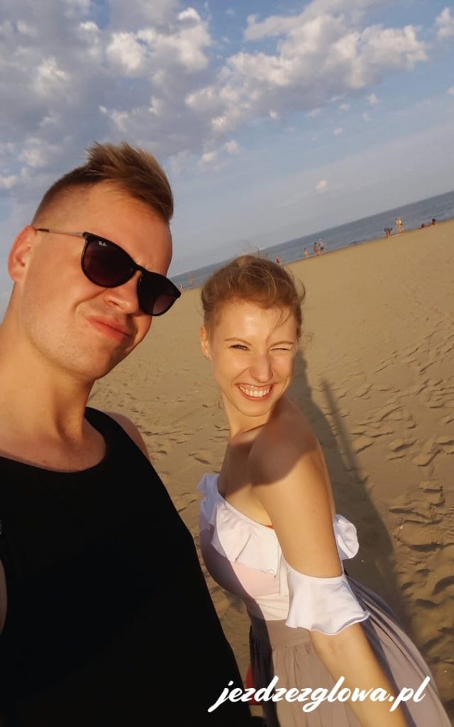 Para turystów robiąca selfie na słonecznej, piaszczystej plaży nad morzem