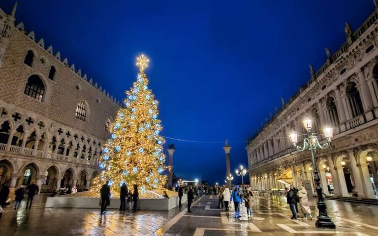 Piazzetta San Marco w Wenecji nocą. Duża choinka oświetlona złotymi światłami między Pałacem Dożów a Procuratie Nuove.