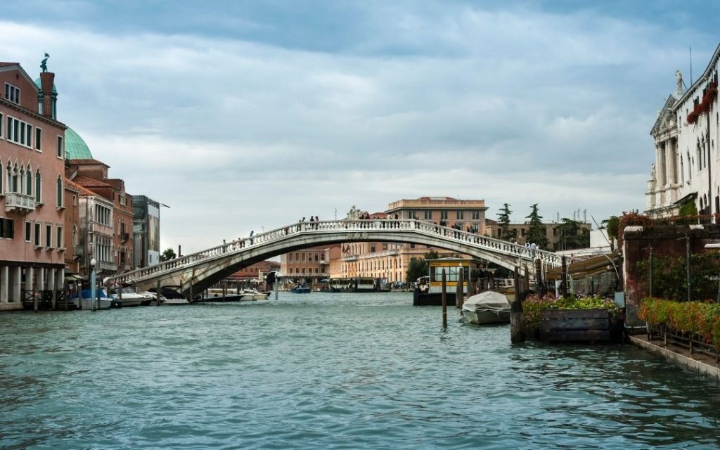 Ponte degli Scalzi duży, kamienny most łukowy nad Canal Grande w Wenecji. Wokół historyczne kamienice pod pochmurnym niebem.