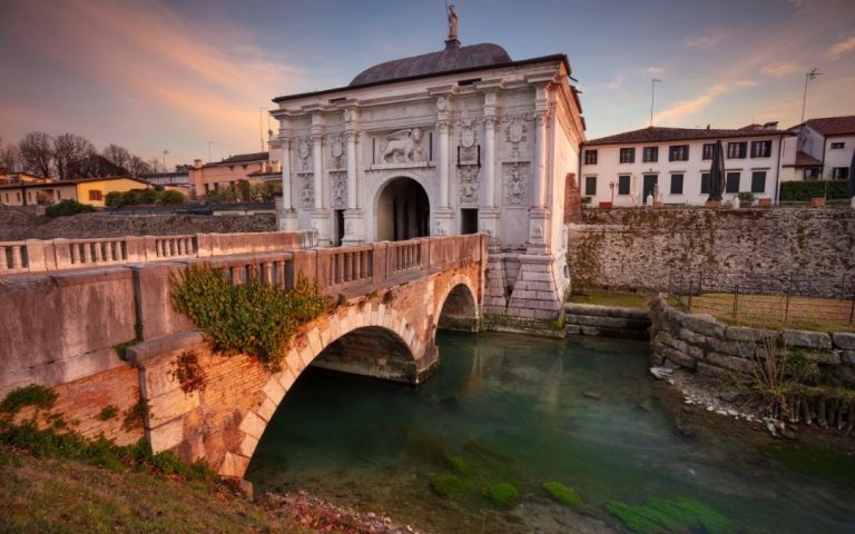 Porta San Tommaso w Treviso. Monumentalna brama obronna z łukiem i pomnikiem lwa, połączona z mostem nad fosą.