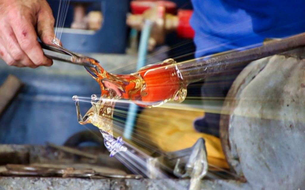Ręce rzemieślnika kształtującego rozgrzane do czerwoności szkło. Dynamiczne ujęcie procesu produkcji szkła z bliska w hucie.