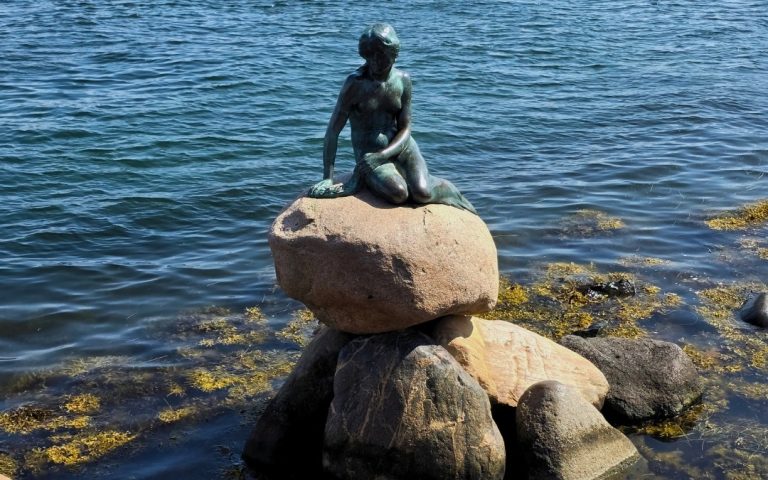 Rzeźba Małej Syrenki siedzącej na kamieniu nad brzegiem portu w Kopenhadze