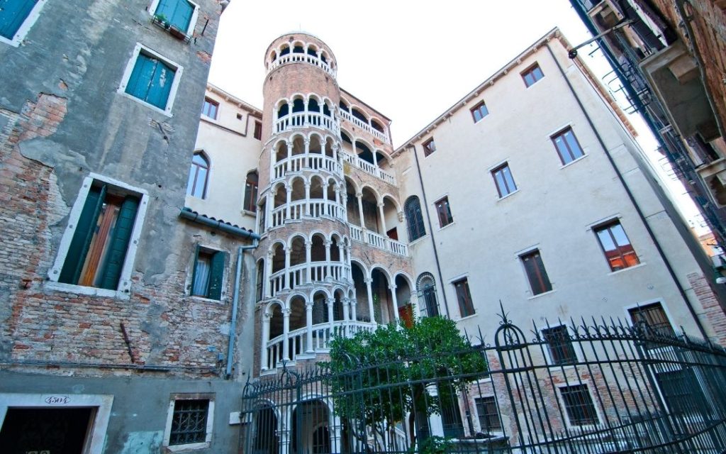 Scala Contarini del Bovolo w Wenecji. Widok z podwórka na spiralną wieżę z łukami, otoczoną historycznymi, wysokimi kamienicami.