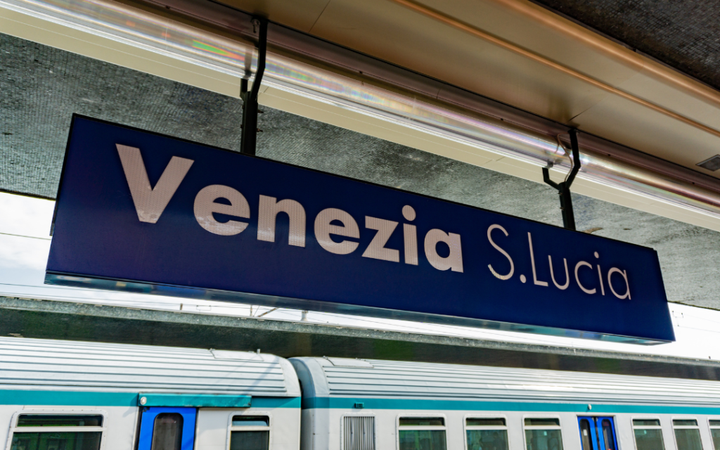 Tablica stacji kolejowej Venezia Santa Lucia wisząca nad peronem z pociągiem w tle