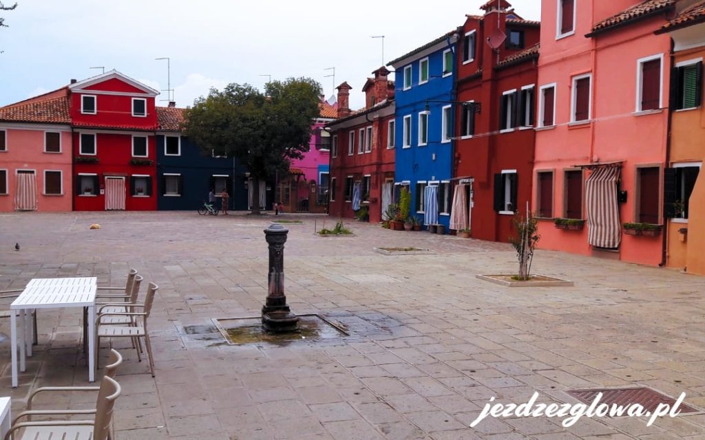 Urokliwy placyk na Burano z czerwonymi i niebieskimi fasadami oraz fontanną
