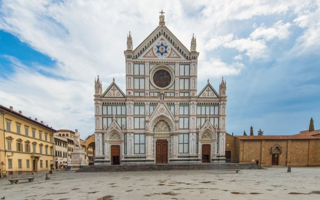 Wielka, neogotycka fasada kościoła w Wenecji, przypominająca marmurową dekorację. Budynek stoi na pustym placu pod zachmurzonym niebem.