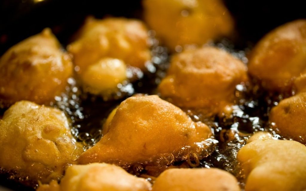Zbliżenie na niewielkie kawałki ciasta (racuchy lub pączki) smażone w głębokim, gorącym oleju. Widać intensywne bąbelkowanie.