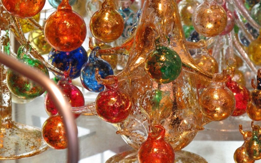 Zbliżenie na szkło z Murano. Złocone, kolorowe, błyszczące bombkiornamenty przymocowane do fragmentu dużej szklanej rzeźby.