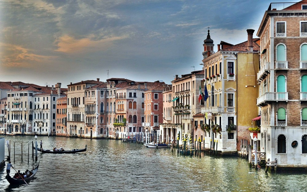 Palazzi przy Canal Grande w Wenecji odbijające się w wodzie, z gondolami płynącymi wzdłuż eleganckich fasad
