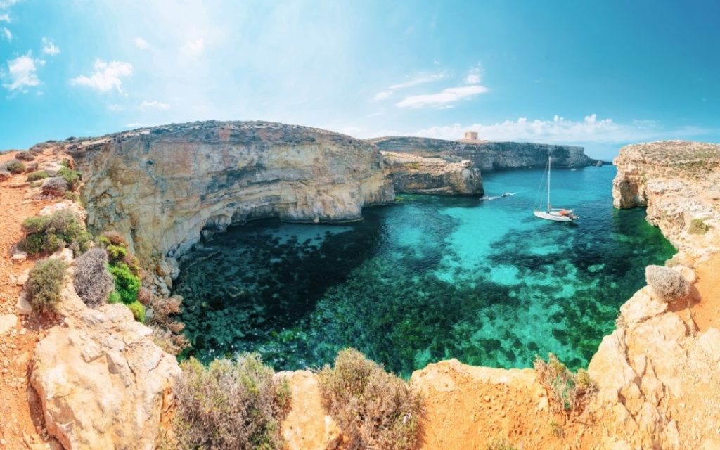 Crystal Lagoon na Malcie, z turkusową wodą, klifami i jachtem na tle malowniczej scenerii