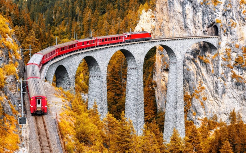Czerwony pociąg Glacier Express na kamiennym wiadukcie Landwasser w Alpach jesienią