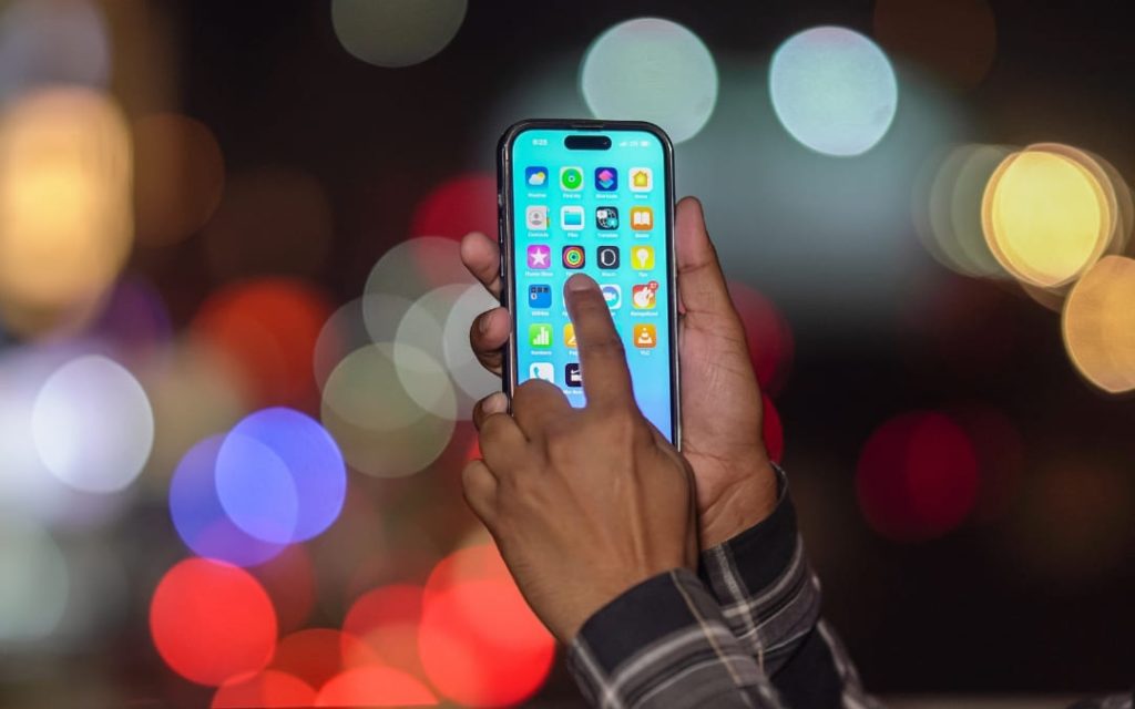 Dłonie trzymające smartfon z ekranem aplikacji na tle kolorowych świateł bokeh nocą