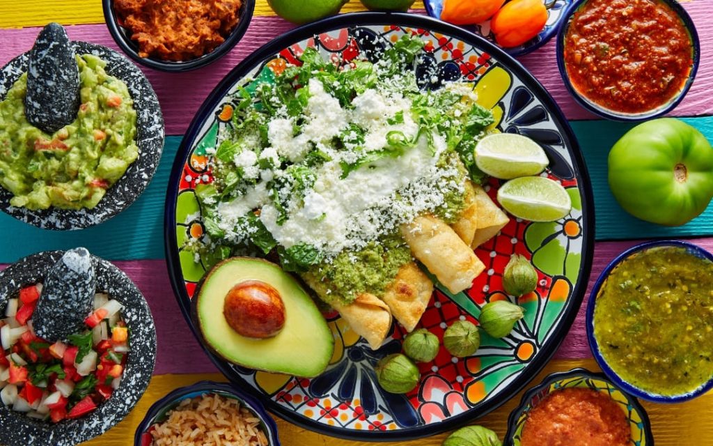 Kolorowy talerz meksykańskich flautas z guacamole, awokado i salsami na stole