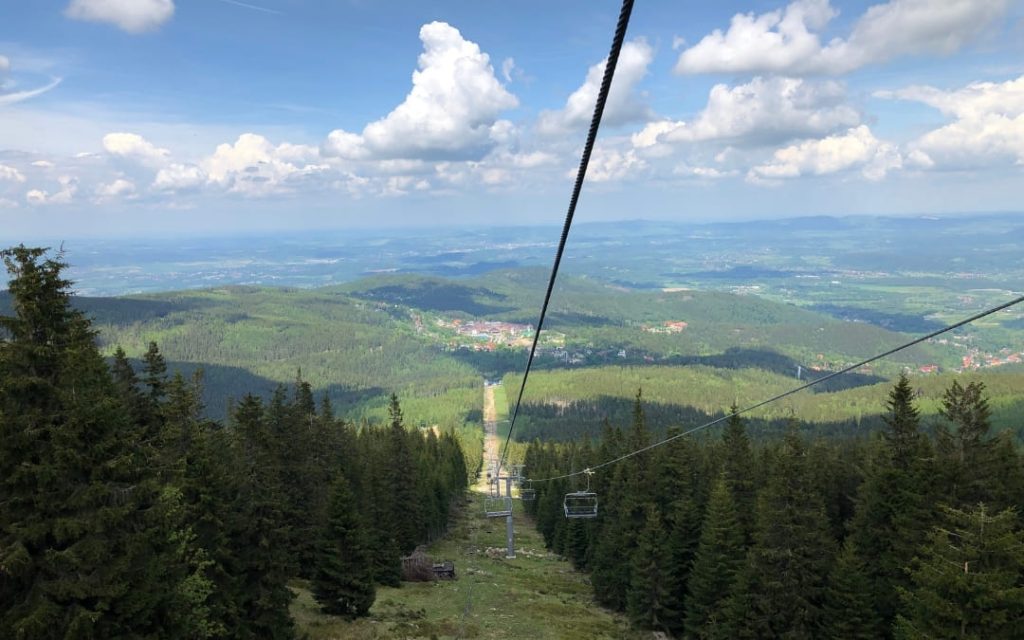 Krzesełka kolei linowej nad lasem świerkowym z panoramą górskiej doliny