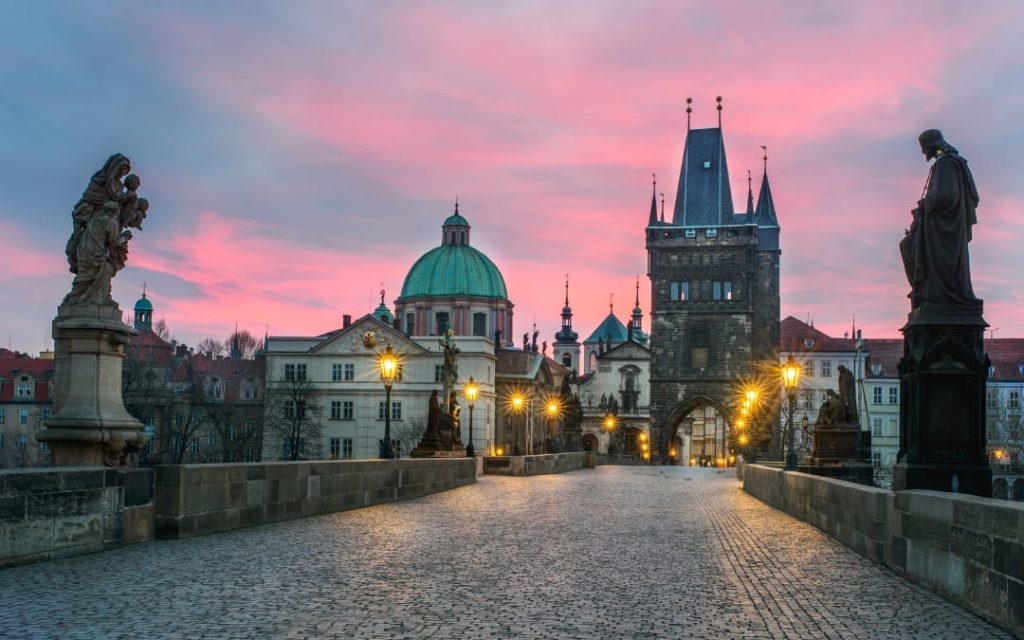Most Karola w Pradze o świcie z posągami świętych i wieżą bramną w różowym niebie