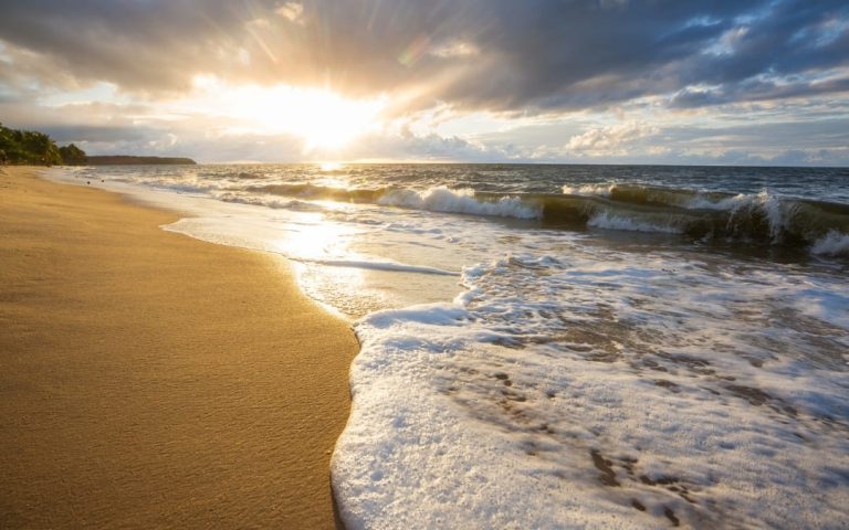 Piaszczysta plaża z falami morskimi i promieniami słońca przebijającymi się przez chmury