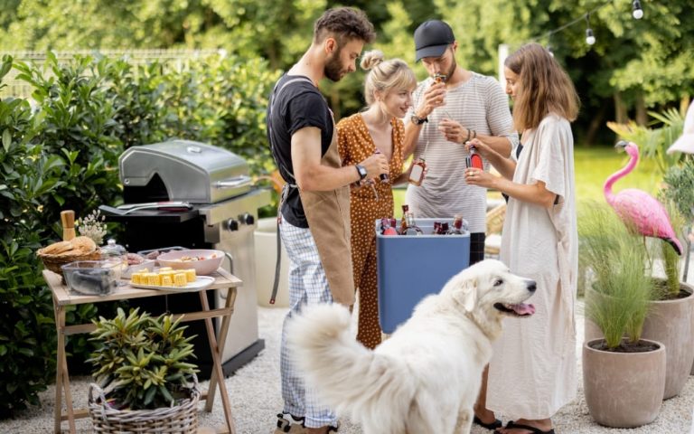 Spotkanie przy grillu w letnim ogrodzie z grupą znajomych i białym psem