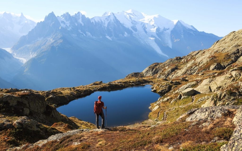 Turysta z plecakiem stojący nad górskim jeziorem na tle masywu Mont Blanc w Alpach