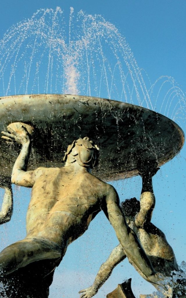 Zbliżenie na rzeźby trzech trytonów podtrzymujących misę