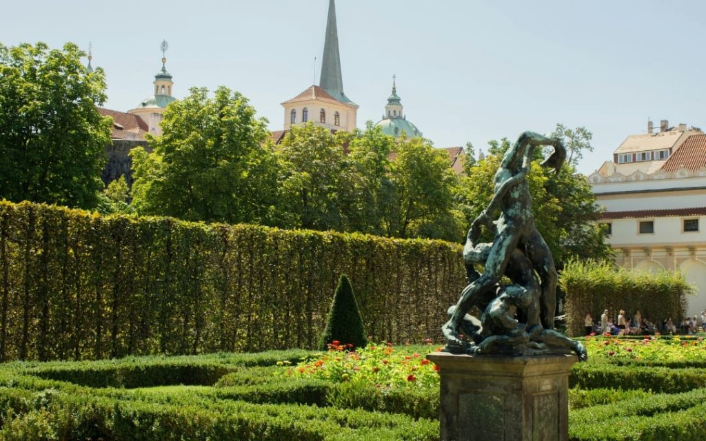 Brązowa rzeźba mitologiczna na cokole w Ogrodach Królewskich z wieżami praskich kościołów w tle