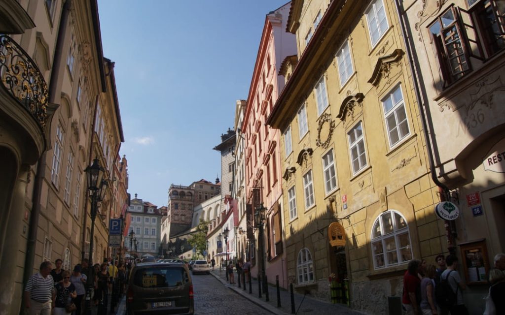 Brukowana uliczka Małej Strany w Pradze z kolorowymi barokowymi kamienicami i przechodniami