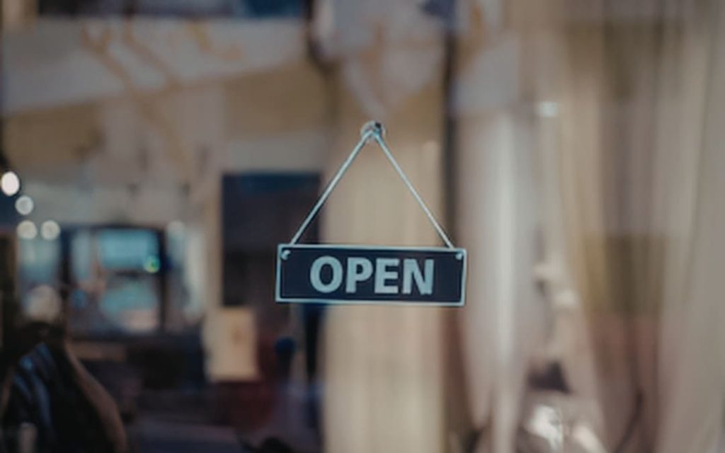 Ciemna tabliczka z napisem Open wisząca na sznurku w drzwiach